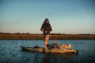 man standing on Kayak at sunset fishing. With kayak cooler closed on back of kayak