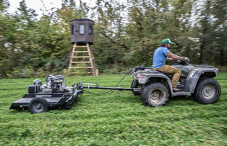 hunting blind on elevated stand in background, with man on 4 wheeler in foreground.