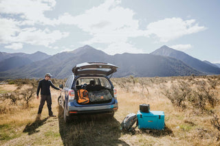 nature is healing, man opening suv with mountains in the background. back hatch of suv is open with outdoor gear and Kenai cooler sitting on ground