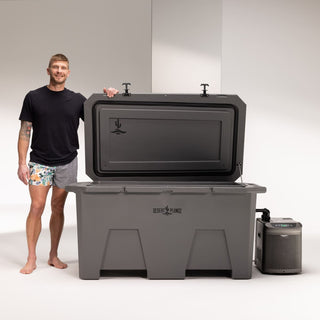 The image shows a man, founder of Desert Plunge, Matt Kuiper, standing next to an open Grizzly cooler which is the company's Exclusive cold plunge offering. The lid is open on the gray cooler with the man resting his hand the lid. You can see the Desert Plunge logo on the lid and centered on the front of the Grizzly cooler. There's a chiller hooked up to the cold plunge.